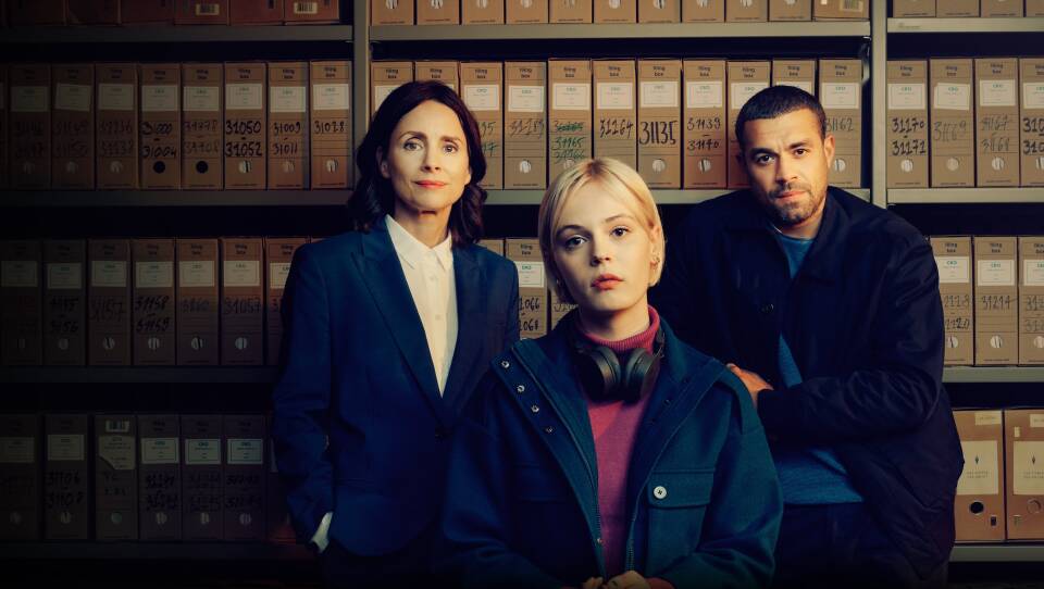 Woman and man standing in front of shelves of file boxes on and a woman with short blond hair sitting in front of them