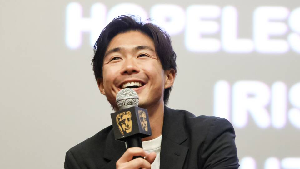 A man smiles and laughs as he holds a microphone on stage at a film screening.
