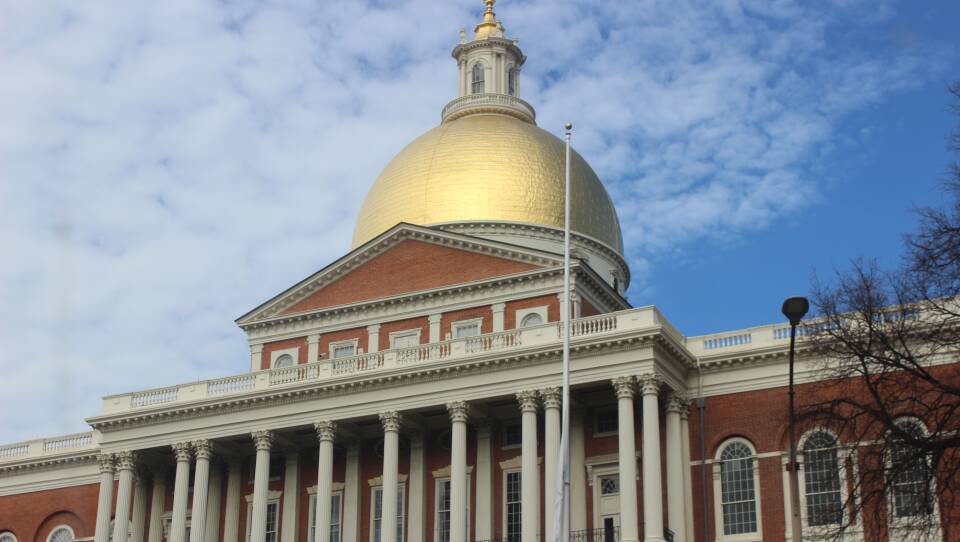 The State House's golden dome shines on a lightly cloudy day.
