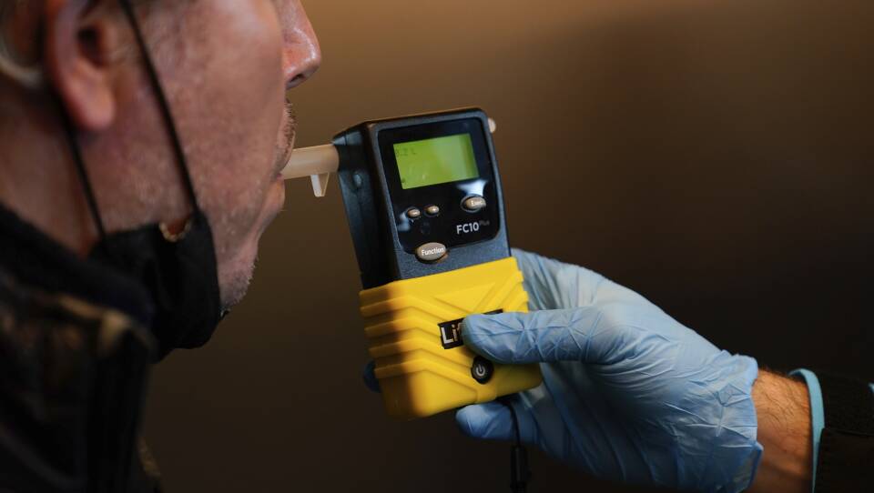 A person blows into a handheld machine with a screen displaying the number 0.2%.