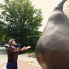 Edgar stands and raises his hands to a large bronze pear statue