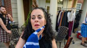 A woman in apparent discomfort holds a wet washcloth against her chin to cool down while standing outside on a hot day.