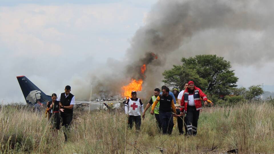 Red Cross workers and rescue workers carry an injured person on a stretcher as airline workers walk away from the site where an Aeromexico airliner crashed in a field near the airport in Durango, Mexico, on Tuesday.