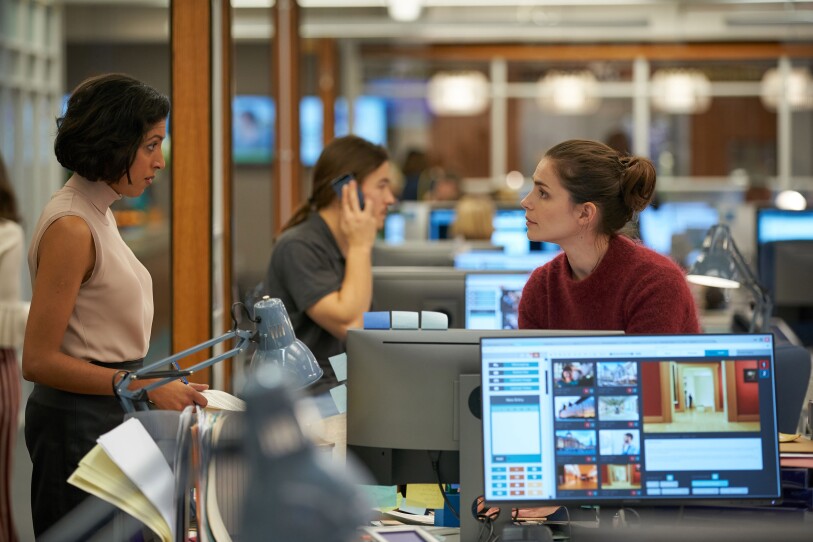 Two women in conversation in the middle of a newsroom