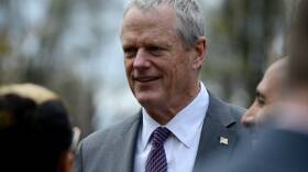 A man in a jacket and tie stands outside in a small group of people.