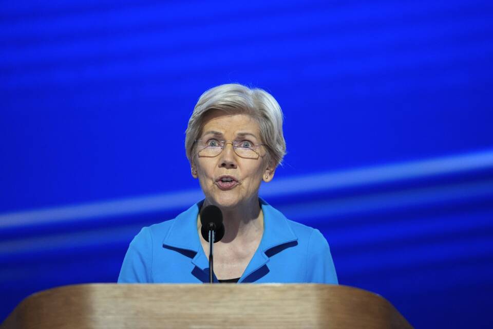 Sen. Elizabeth Warren speaks from behind a podium on stage, with a blue background behind her.