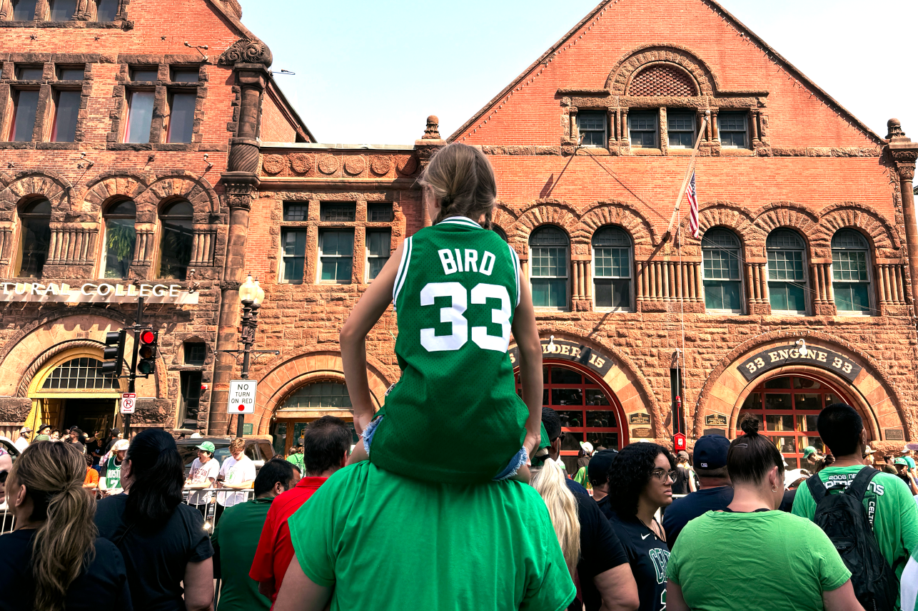 A young girl in a Larry Bird jersey sits someone's shoulders ahead of the Celtics parade.
