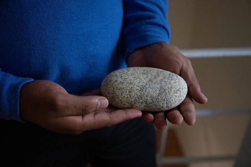 A pair of hands holding a round rock, roughly the size of a palm.