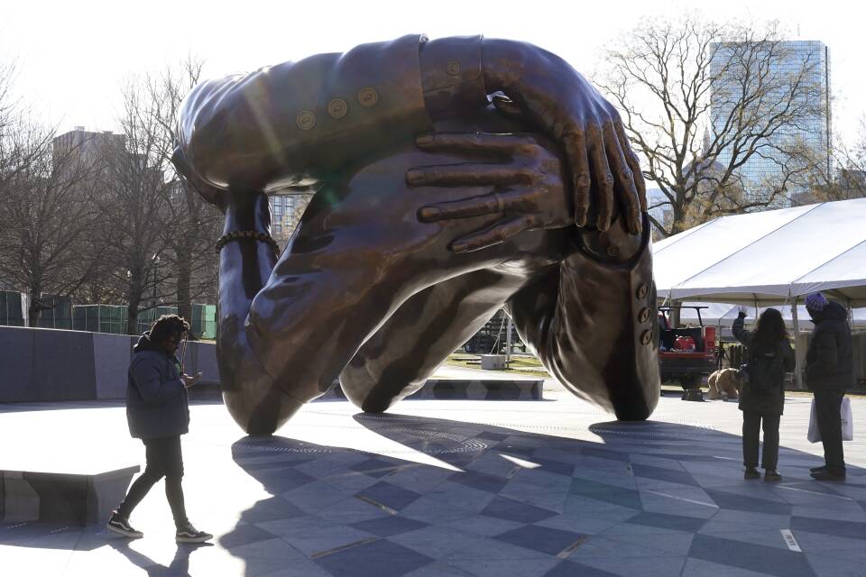 People stand in the shadows of a large abstract sculpture of two people embracing.
