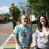 Two people laugh and smile, posing in front of a rainbow-painted crosswalk