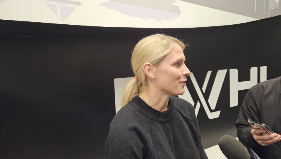 A woman in a black shirt stands in front of a black wall with a PWHL logo in white on it