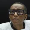Close-up on a woman wearing a blazer and heavily rimmed square glasses. She looks pensive.