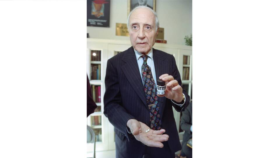 A man in a suit posing with a bottle marked RU 486 and two small white pills in his hand.