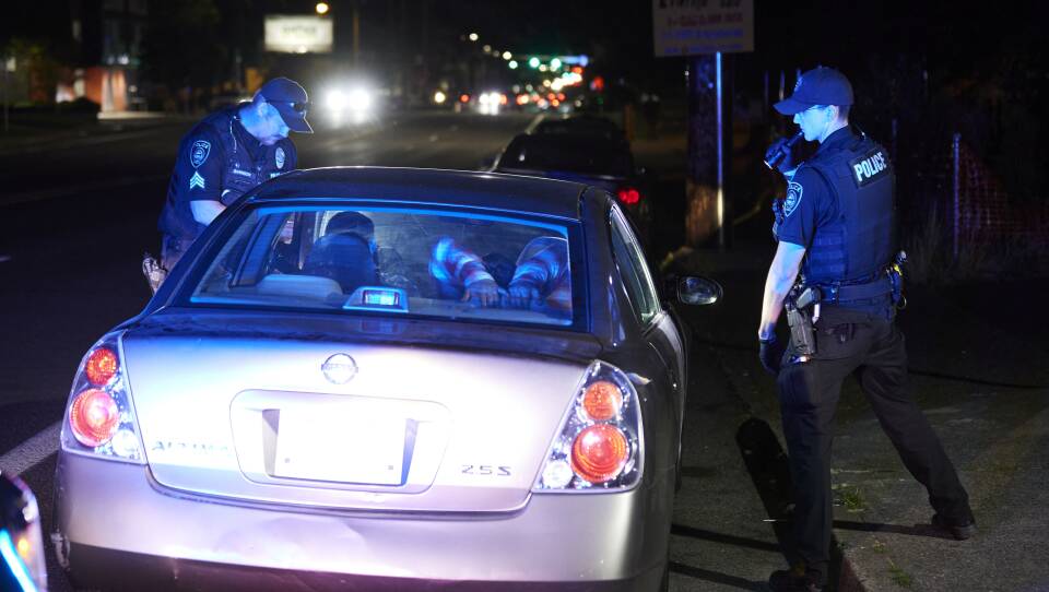 Two officers approach a sedan in the evening.