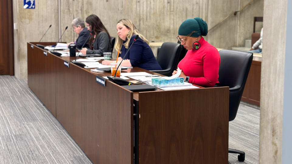 Four councilors are seated in the chamber in their office chairs.