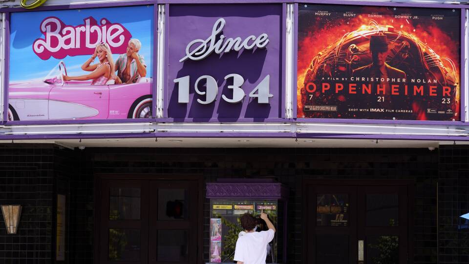A person buys a ticket at an old-school movie theater, which has posters for "Barbie" and "Oppenheimer"