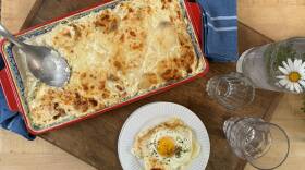 Red casserole dish with a potato gratin next to a plate of gratin topped with an egg