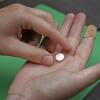 A patient holds a small white pill stamped "MF" in her hand.