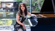 Yoko Miwa wears a flower patterned dress, and sits at a grand piano in front of beautiful garden with pond.
