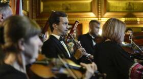 A man playing the clarinet is the focus of this photo, where he's surrounded by fellow members of the orchestra playing instruments like violins and oboes.