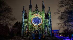 A large chapel is lit up in orange, green, and blue at night by a projection.