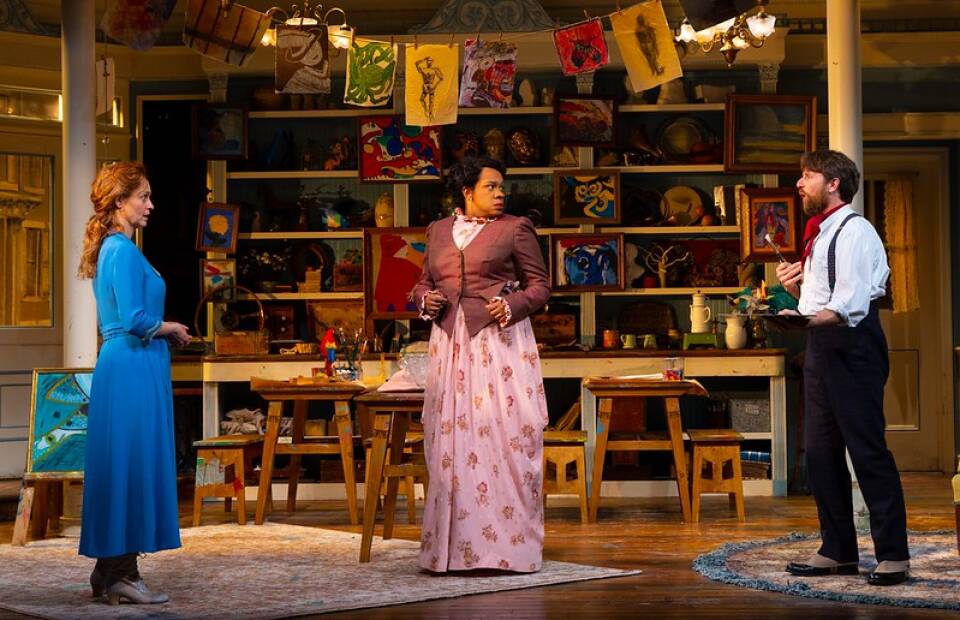Three actors stand wearing antiquated clothing in an art studio during the Huntington's production of "Joy and Pandemic." They seem to be in a heated conversation, with the two women looking with concern at the man on the far right