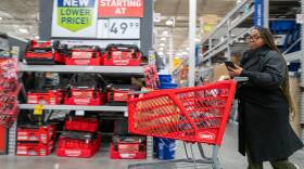 A woman pushes a shopping cart past a display with signs that read "new lower price! Starting at $49.99"