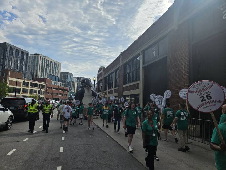Workers demonstrate as a large inflatable rat looms in the background.