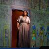 African-American woman in a beige empire-waist dress stands in front of a wall of Egyptian drawings