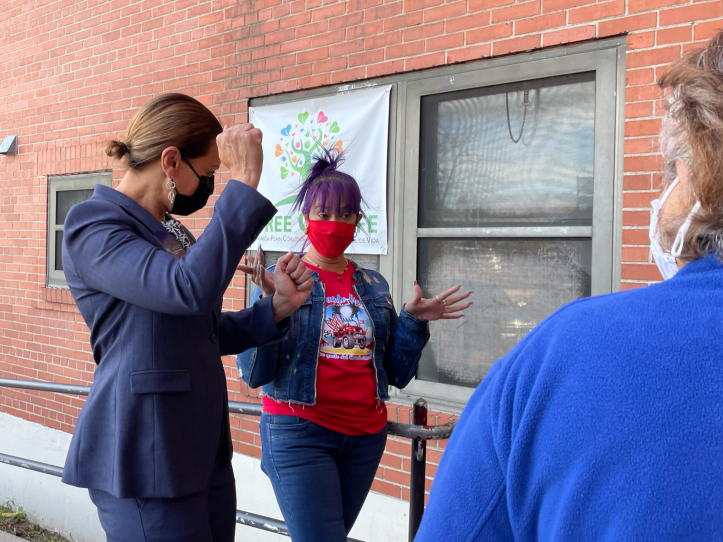 woman wearing mask and navy pantsuit pumps her fist while talking to a shorter woman with a bright red mask and purple hair