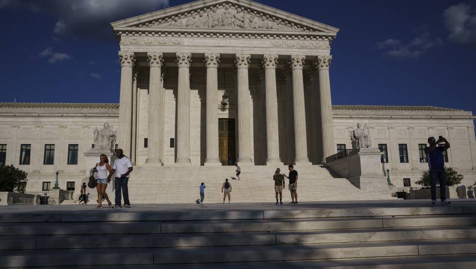 About 10 people walk past and take photos on the steps outside the U.S. Supreme Court.