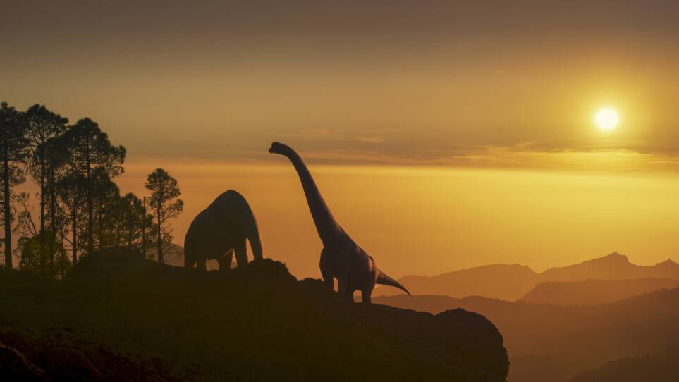 Long-necked dinosaurs on a mountain ledge in front of a yellow sky