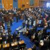 Lawmakers stand at their desks and applaud in the Massachusetts House chamber, a wood-paneled, blue-carpeted room.