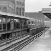 A black-and-white photo of a subway train pulling into a station, with a few people on the platform waiting for it.