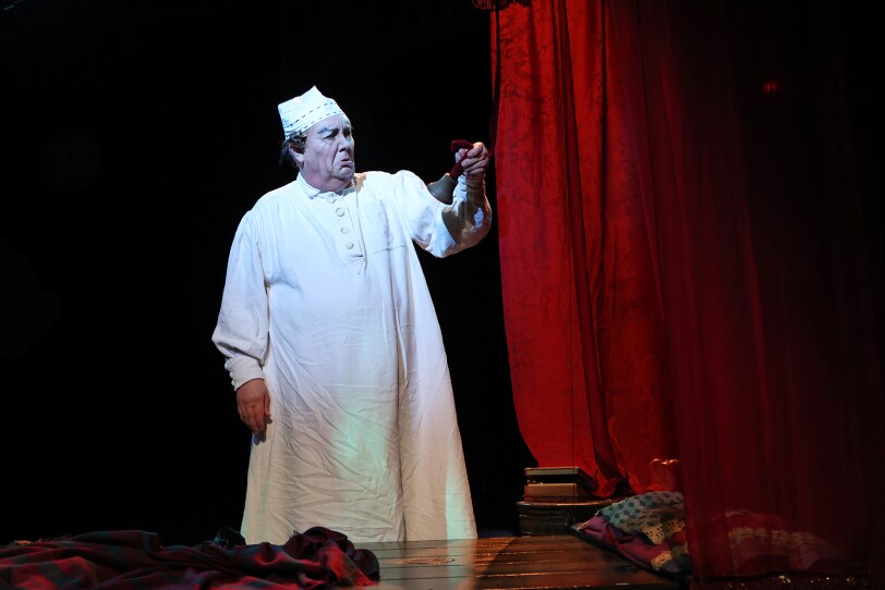David Coffee performs as Scrooge, in a nightgown and nightcap while holding a candle, in North Shore Music Theatre's production of "A Christmas Carol"