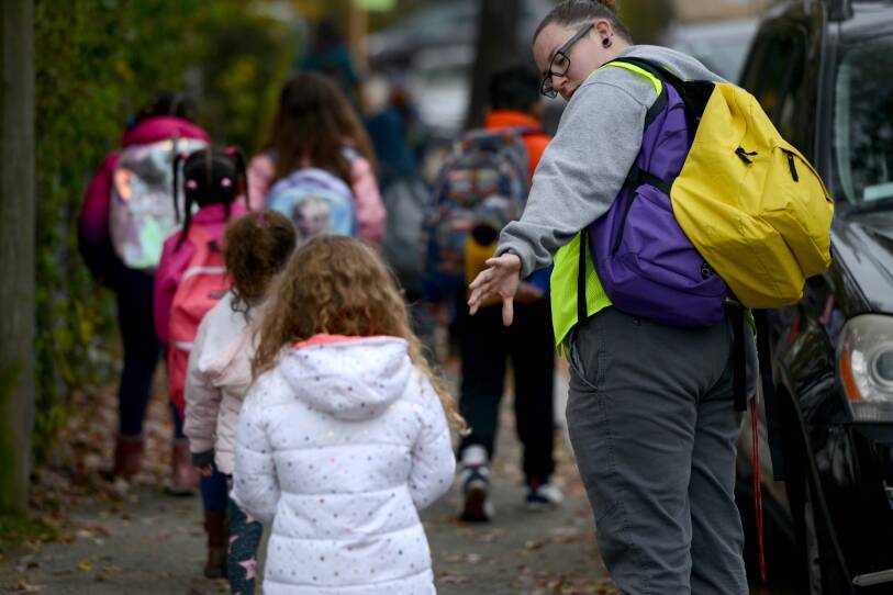 A woman reaches out her hand to a girl walking behind her on a sidewalk. A line of other students are in front of them.