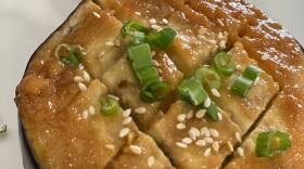 Rounds of eggplant with a glaze on top, sprinkled with sesame seeds and scallions