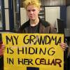 A person holds a yellow sign that reads 'My grandma is hiding in her cellar'