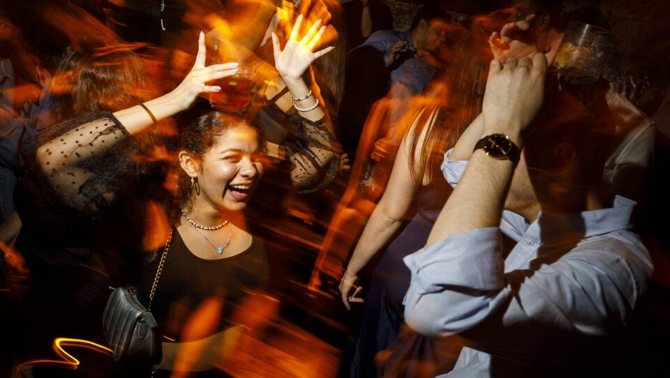A women dances and smiles in a crowded nightclub surrounded by people.