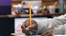 A Black student writes with a pencil at their desk in a classroom
