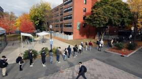 A long time of people standing near a large brick residential building.