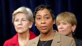 Campbell wears a blazer and looks out seriously. She’s flanked by women standing in the background.