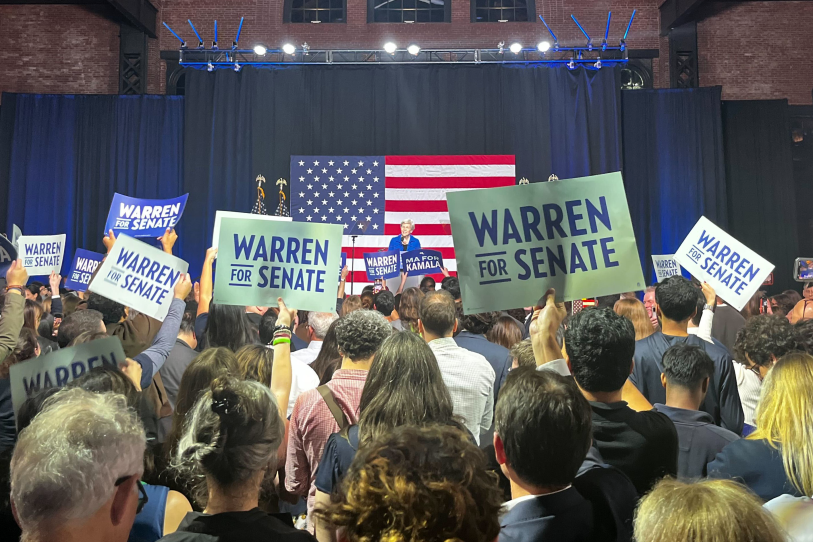 Warren speaks from a far-away podium on stage, with hundreds of supporters between the photographer and the senator. A massive American flag hangs behind her.