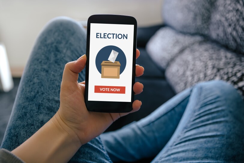 A person sits cross legged and holds a smartphone in their hand with an election voting app on the screen.