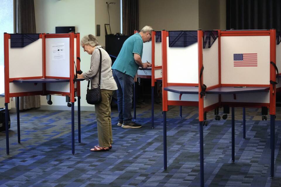 Two people stand at tables separated by privacy screens as they mark their ballots.