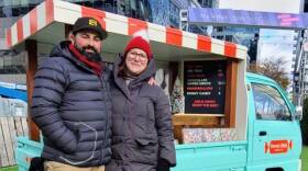 A couple stand in front of a blue candy truck.