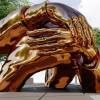 A large bronze sculpture of hands wrapped around each other sits in the center of a park.