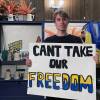 A man stands holding a sign that says 'Can't take our freedom'