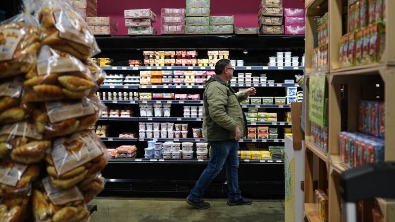 A man reaches for what looks like yogurt in a well-stocked grocery store.