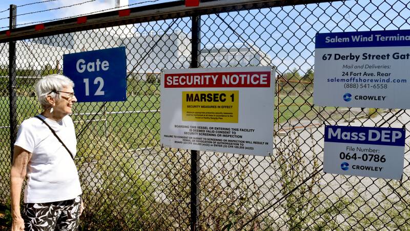 An older woman looks through a chain-link fence.